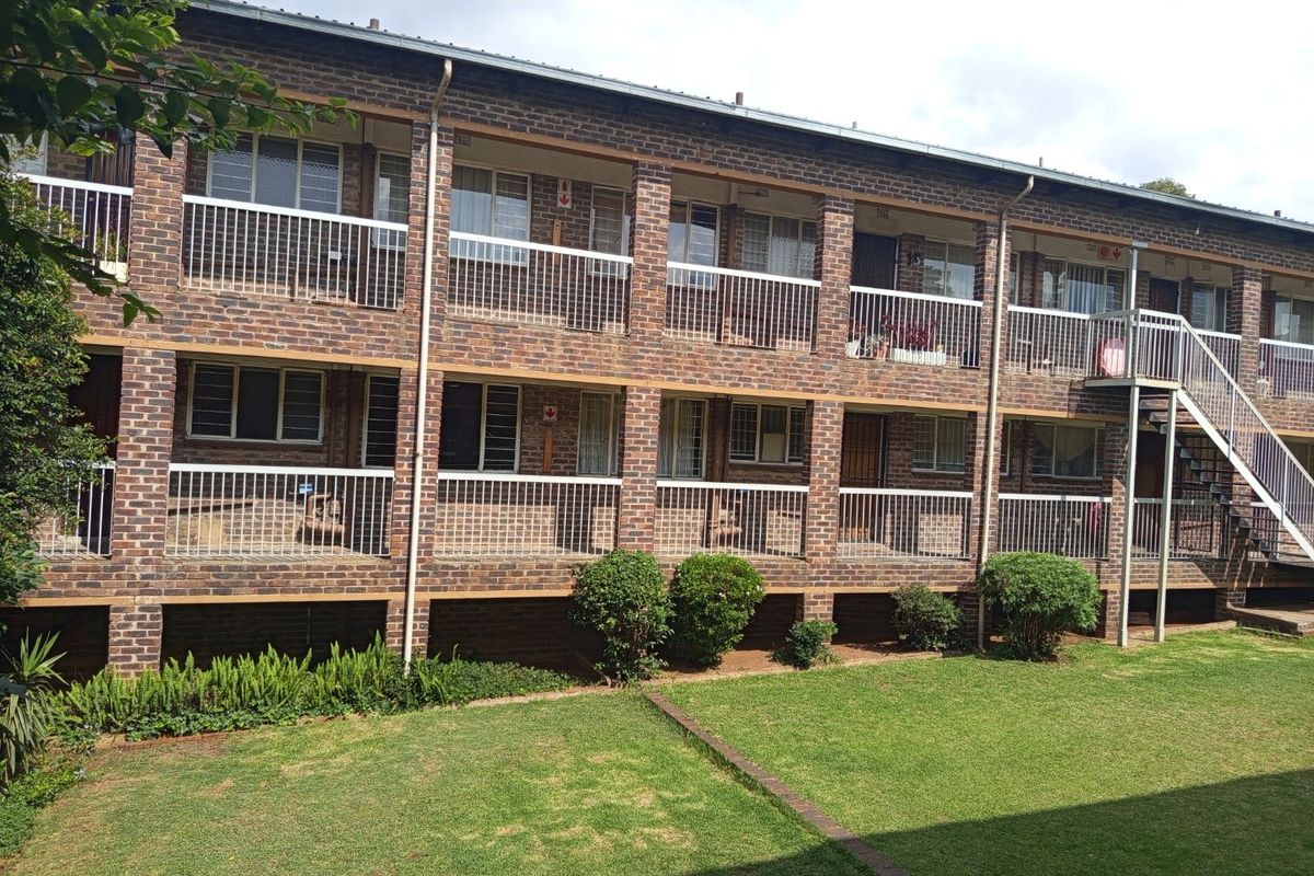 Rear view of a multi-story apartment complex featuring face brick construction, metal balustrades, and access to a communal garden area.