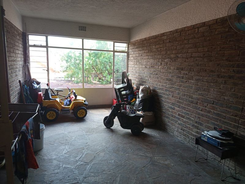 A covered patio area featuring exposed brick walls and durable stone flooring, offering a versatile outdoor space with large windows.