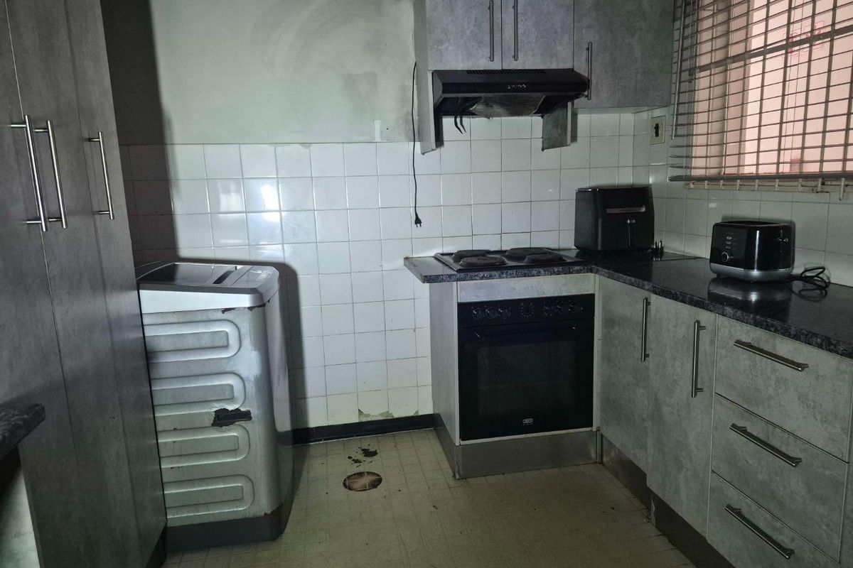 A compact kitchen featuring built-in cabinetry, an electric oven and hob, and a tiled backsplash, currently requiring maintenance and cosmetic updates.