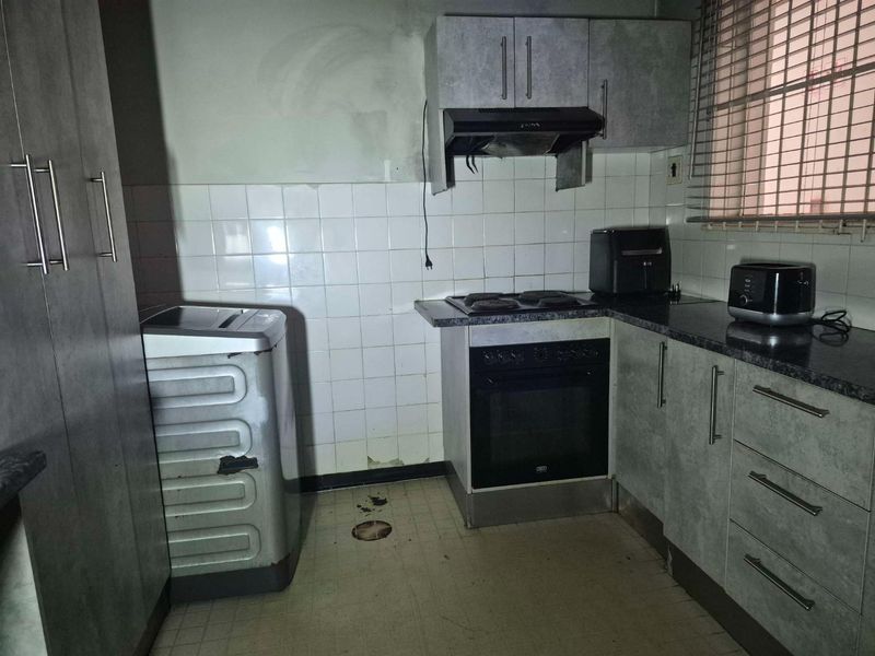 A compact kitchen featuring built-in cabinetry, an electric oven and hob, and a tiled backsplash, currently requiring maintenance and cosmetic updates.