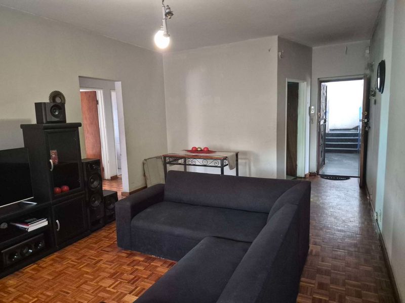 Living room featuring traditional parquet flooring and direct access to the apartment entrance, offering a functional space with potential for cosmetic updates.