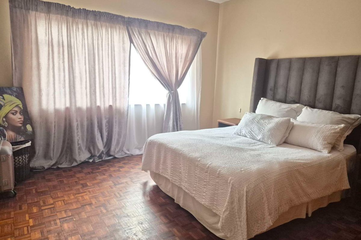 A bedroom featuring classic parquet flooring and large windows with curtains, providing a neutral space ready for personalization.