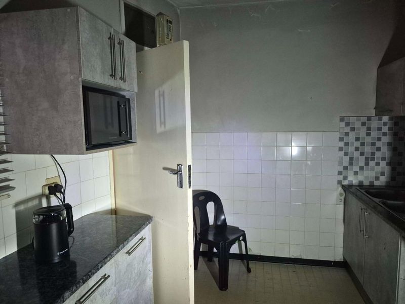 A dated kitchen featuring laminate countertops, tiled splashbacks, and built-in cabinetry, requiring cosmetic updates to improve its overall condition and appeal.