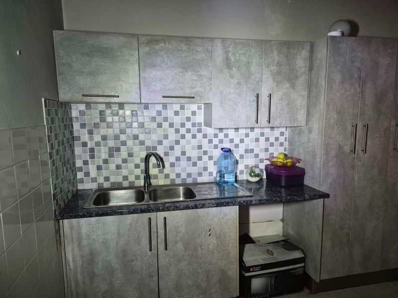 A functional kitchen area featuring grey textured cabinetry, a double stainless steel sink, and a decorative mosaic tile backsplash.