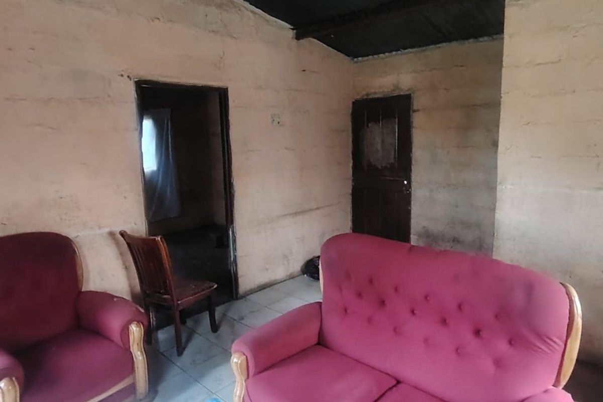 A living room space featuring tiled flooring and exposed ceiling beams, currently requiring significant renovation and cosmetic updates to improve the interior condition.