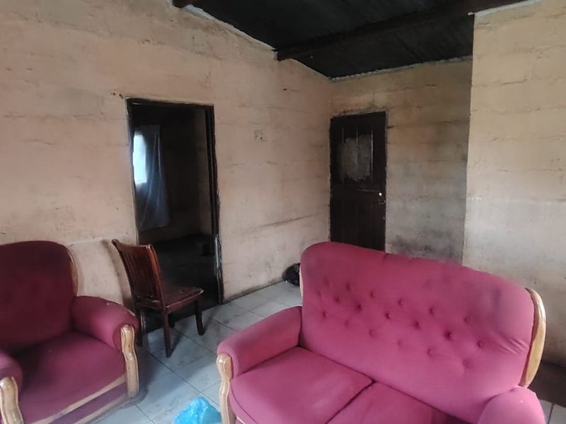 A living room space featuring tiled flooring and exposed ceiling beams, currently requiring significant renovation and cosmetic updates to improve the interior condition.