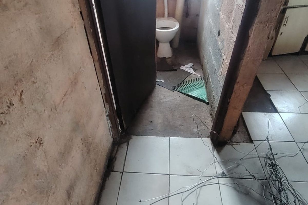 A small, unfinished bathroom space featuring a toilet, exposed brick walls, and incomplete floor tiling, requiring significant renovation and finishing work.