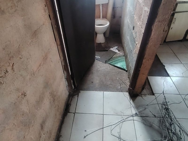 A small, unfinished bathroom space featuring a toilet, exposed brick walls, and incomplete floor tiling, requiring significant renovation and finishing work.