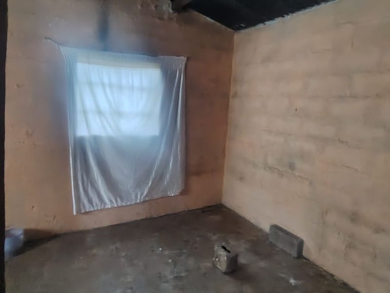 A basic, unfinished bedroom featuring exposed brick walls, a concrete floor, and a corrugated iron roof structure.