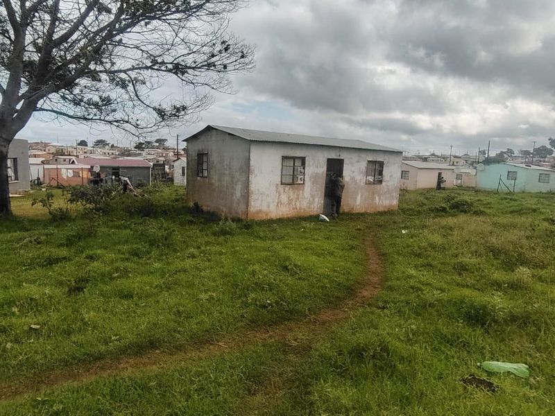 A detached single-story residential structure featuring a corrugated metal roof and weathered exterior walls, situated on a large grass plot.
