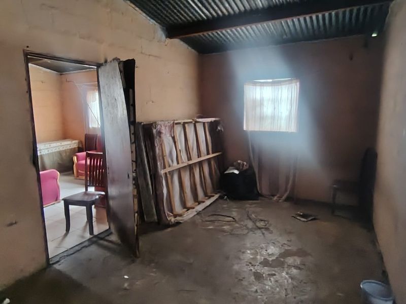 A basic, unfinished bedroom featuring exposed corrugated iron roofing, masonry walls, and a concrete floor, offering a blank canvas for renovation.