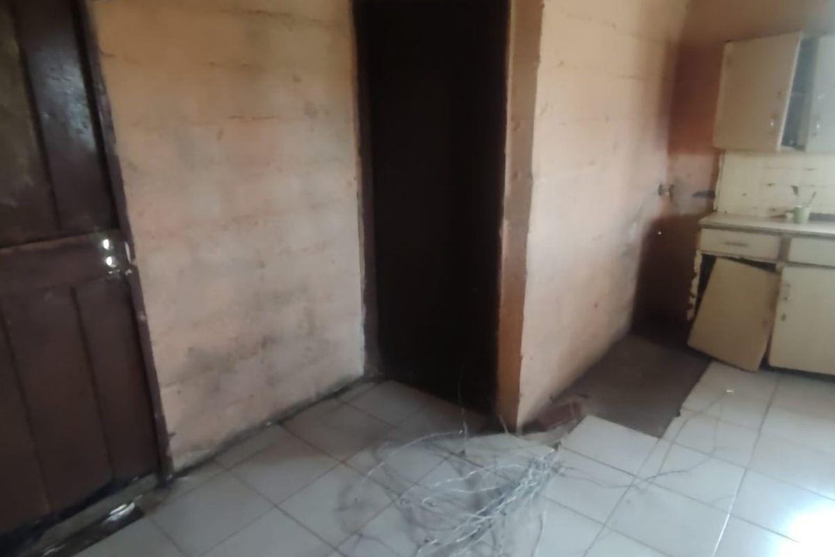 A small, dated kitchen area featuring tiled flooring and built-in cabinetry, currently in need of significant renovation and repair.