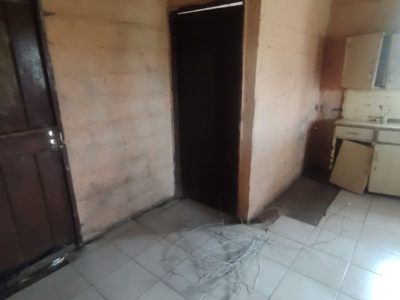 A small, dated kitchen area featuring tiled flooring and built-in cabinetry, currently in need of significant renovation and repair.