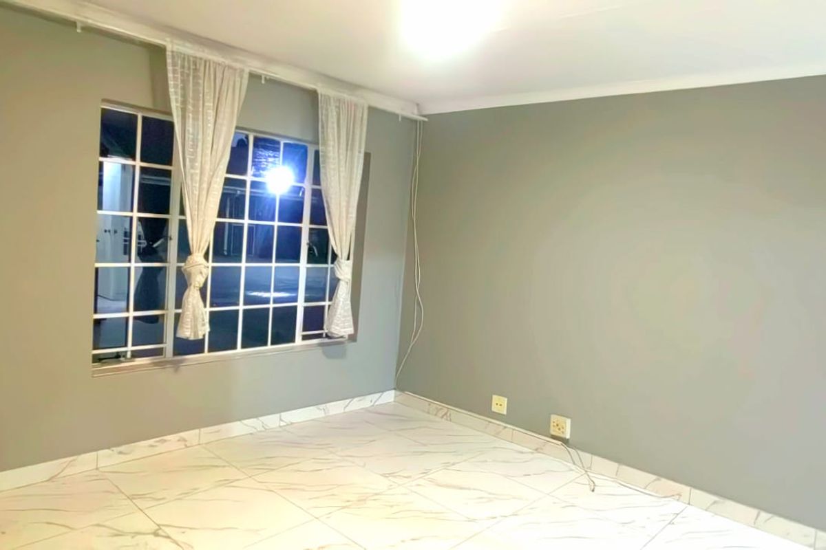 A bright, empty bedroom featuring modern marble-look tiled flooring, neutral grey walls, and a large grid-pattern window allowing for natural light.