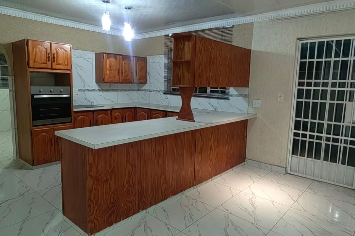 Spacious kitchen featuring built-in wooden cabinetry, marble-look floor tiles, and a breakfast bar, offering a functional layout with direct access to the exterior.