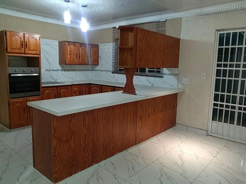 Spacious kitchen featuring built-in wooden cabinetry, marble-look floor tiles, and a breakfast bar, offering a functional layout with direct access to the exterior.