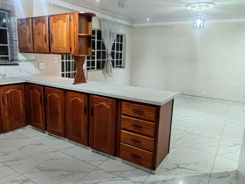Open-plan kitchen and living area featuring wooden cabinetry, marble-look tiled flooring, and security bars on windows.