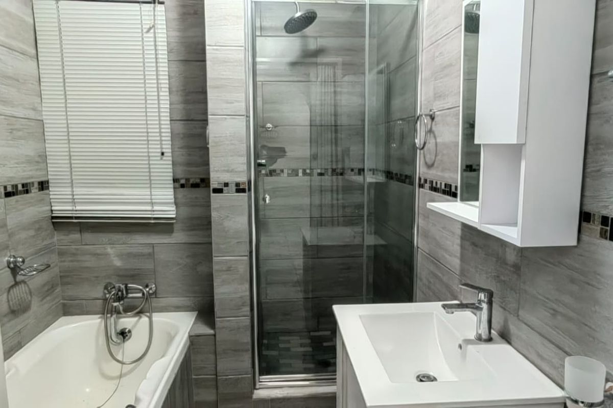 Modern bathroom featuring a bathtub, separate glass-enclosed shower, vanity basin with storage, and contemporary grey wood-look wall tiling.