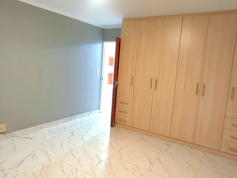 A bright, empty bedroom featuring modern marble-look floor tiles and extensive built-in wooden cupboards, offering ample storage space.