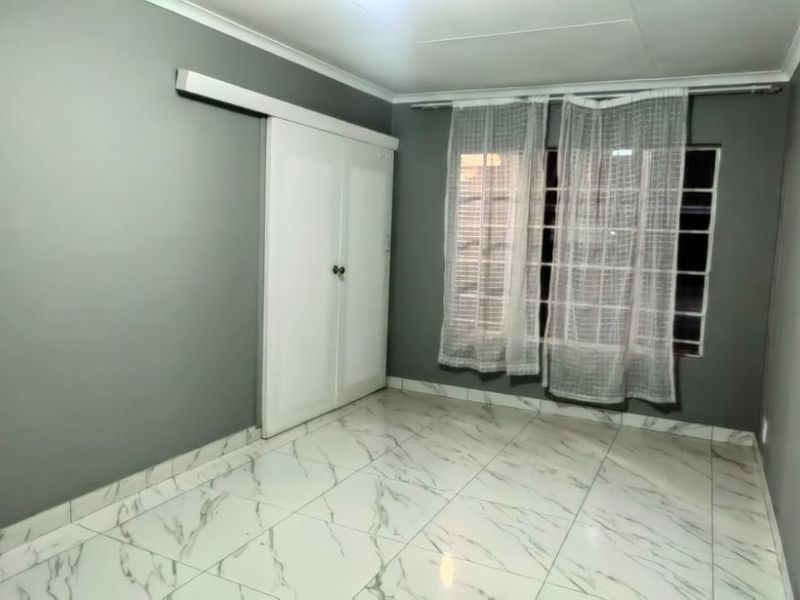 A clean, empty bedroom featuring modern marble-look tiled flooring, grey painted walls, and a built-in sliding door wardrobe.