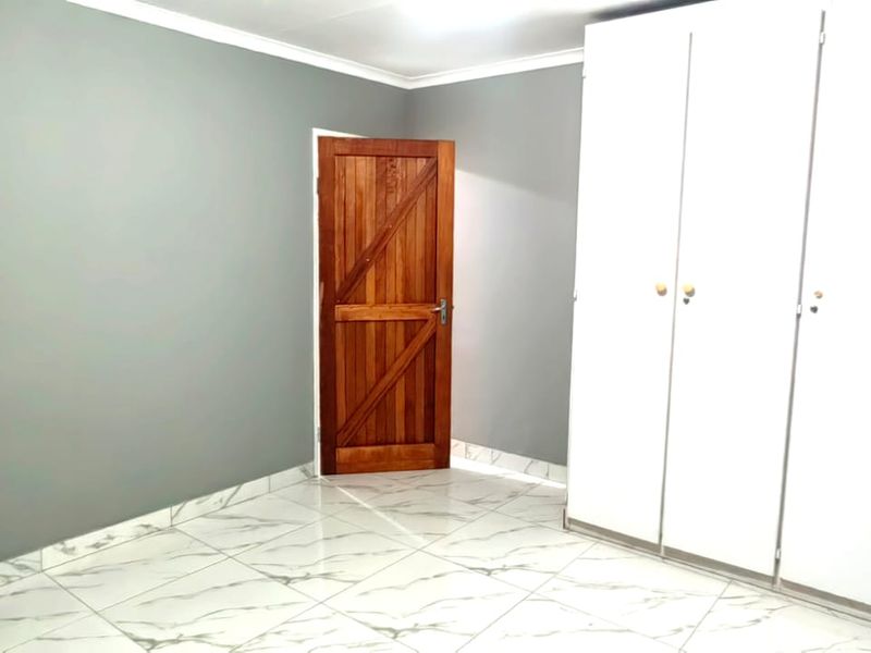 A clean, empty bedroom featuring modern marble-look tiled flooring, grey painted walls, and a large white built-in wardrobe with a classic wooden door.