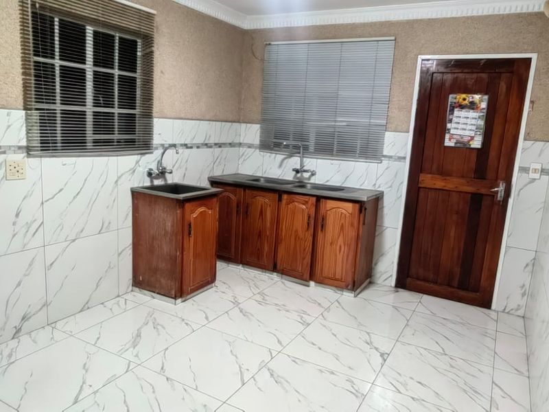 A functional kitchen area featuring marble-look wall and floor tiling, wooden cabinetry, and dual sink stations, providing a clean and practical utility space.