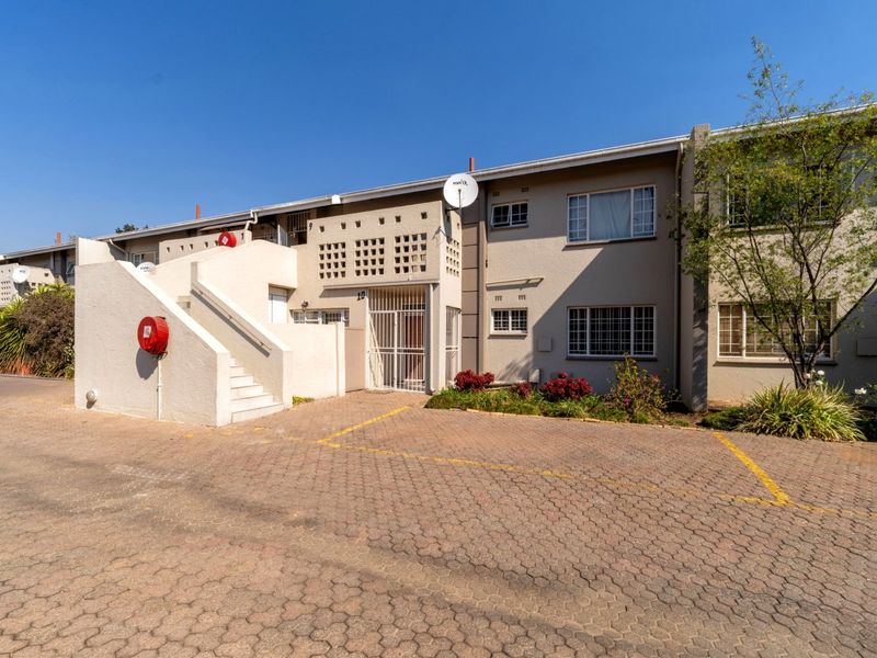 Front elevation of a multi-story apartment complex featuring a paved driveway, external staircase, and security-gated entrance.