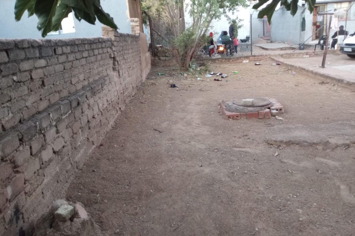 A rear yard area featuring a brick boundary wall and an exposed manhole cover, offering potential for landscaping and outdoor improvement.