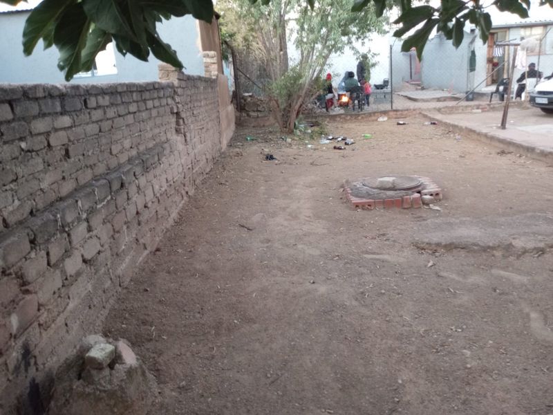 A rear yard area featuring a brick boundary wall and an exposed manhole cover, offering potential for landscaping and outdoor improvement.