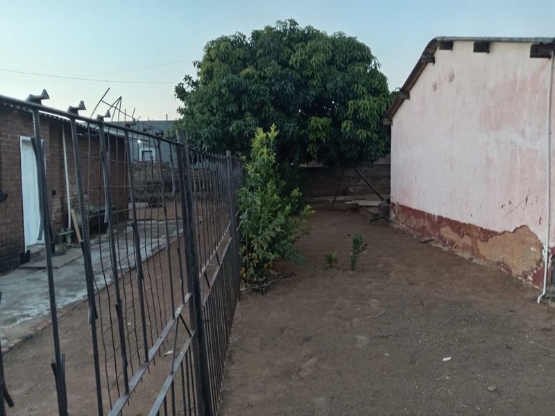 A view of the rear exterior area featuring a metal fence, concrete pathway, and a building with visible exterior wall surface deterioration.