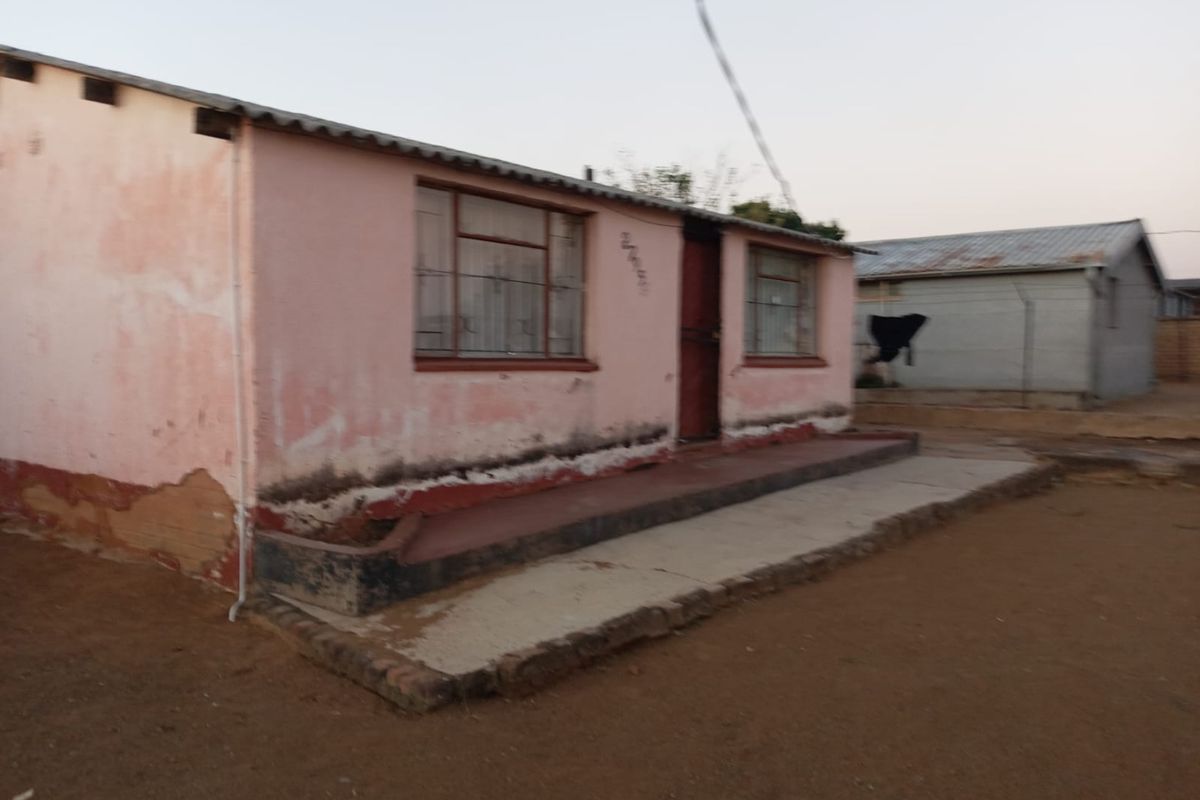 A single-story residential dwelling featuring a concrete porch and corrugated metal roof, showing significant signs of exterior wear and weathering.