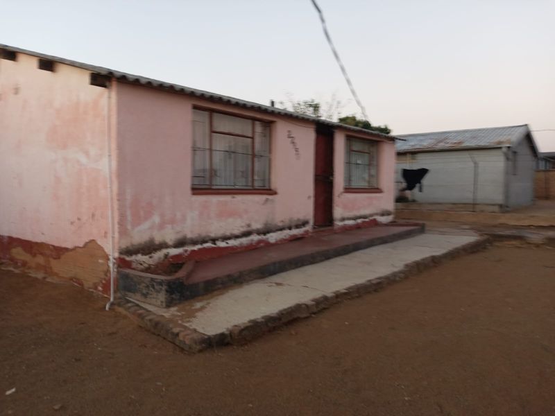 A single-story residential dwelling featuring a concrete porch and corrugated metal roof, showing significant signs of exterior wear and weathering.