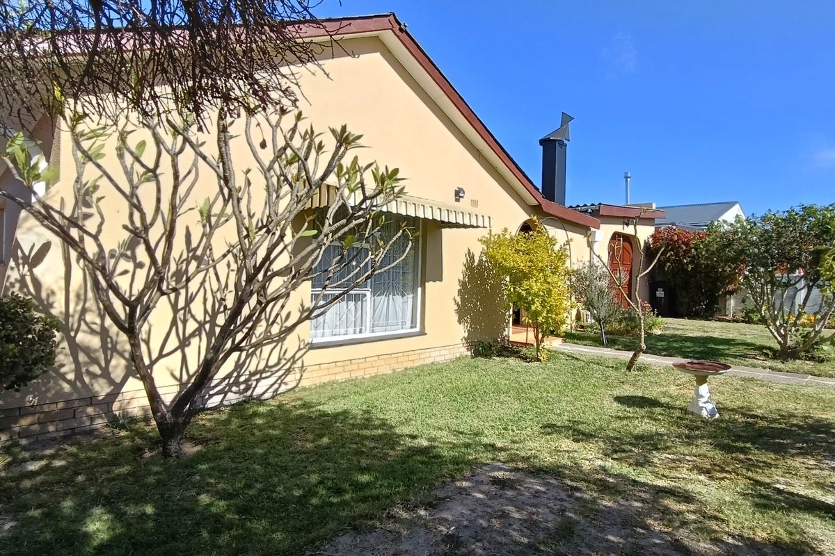 A view of the rear exterior of the house featuring plastered walls, a chimney, and a well-maintained garden area.