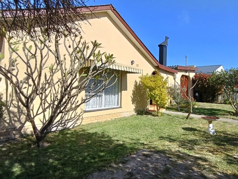 A view of the rear exterior of the house featuring plastered walls, a chimney, and a well-maintained garden area.