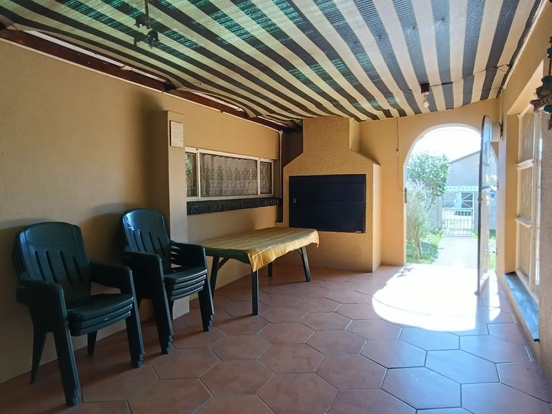 A covered patio area featuring a built-in braai, tiled flooring, and direct access to the garden through an arched doorway.
