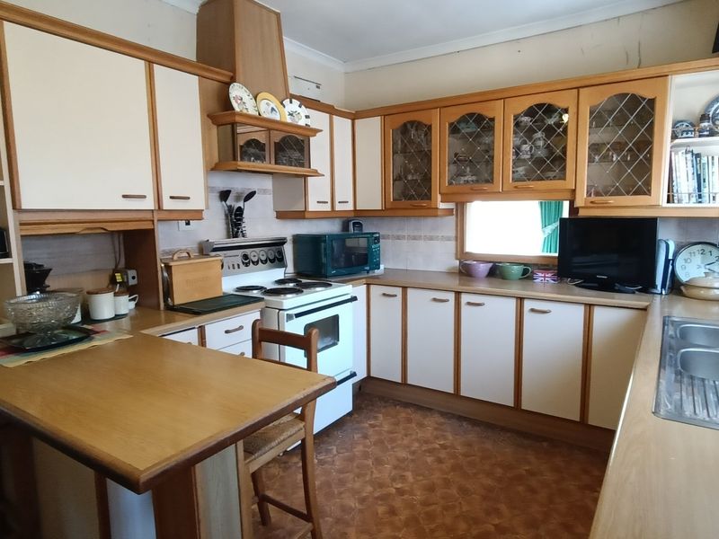 A dated kitchen featuring traditional laminate cabinetry, a double bowl stainless steel sink, and a freestanding oven, offering significant potential for modern renovation.