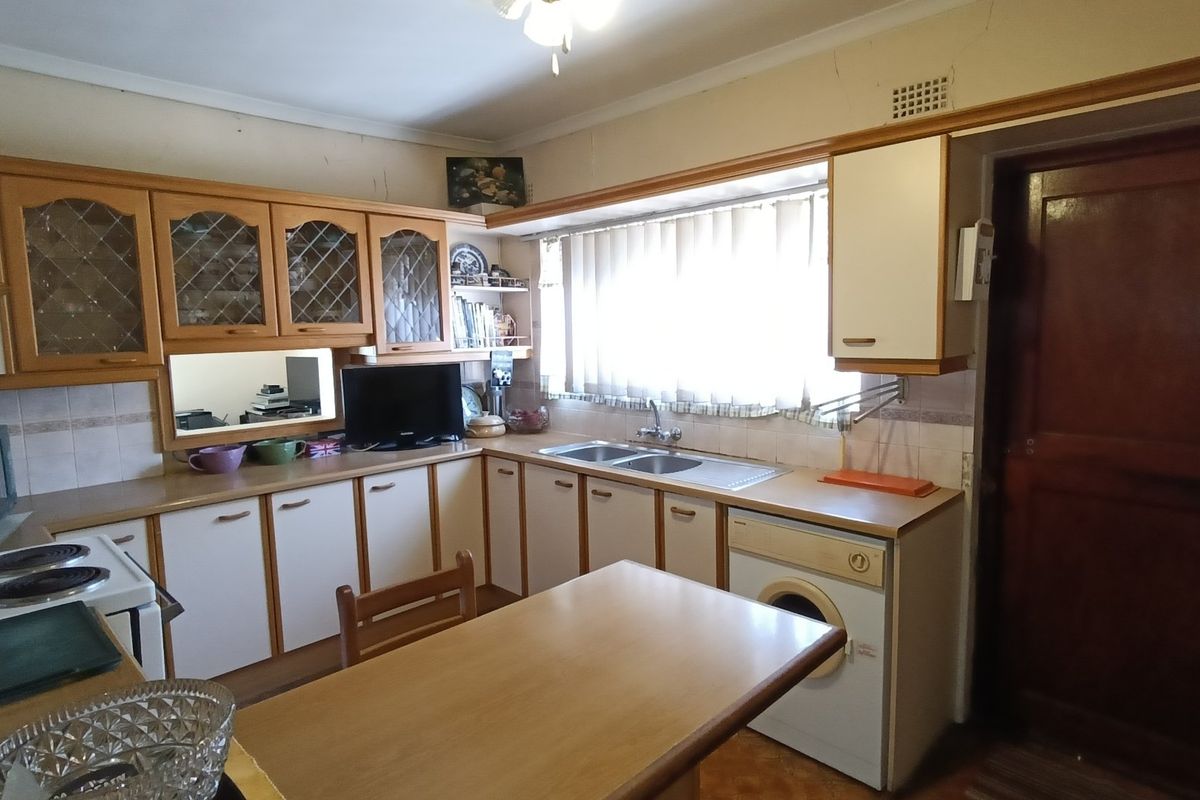 A dated kitchen featuring laminate cabinetry, a double bowl sink, tiled backsplash, and integrated laundry facilities, requiring cosmetic updates to modernize the space.