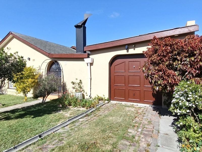 Front elevation of a single-story house featuring a single garage, paved driveway, and an arched window with security gate.