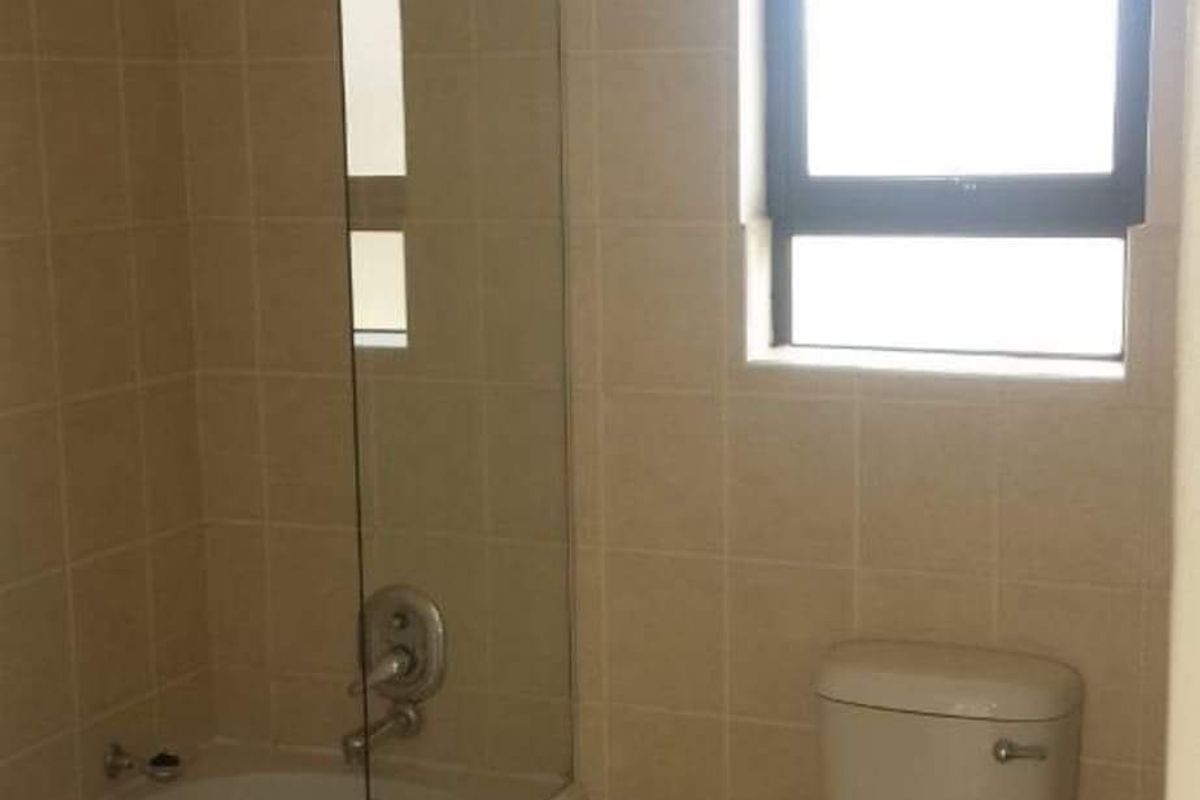 A functional bathroom featuring a bathtub with a glass shower screen, tiled walls, and a standard toilet.