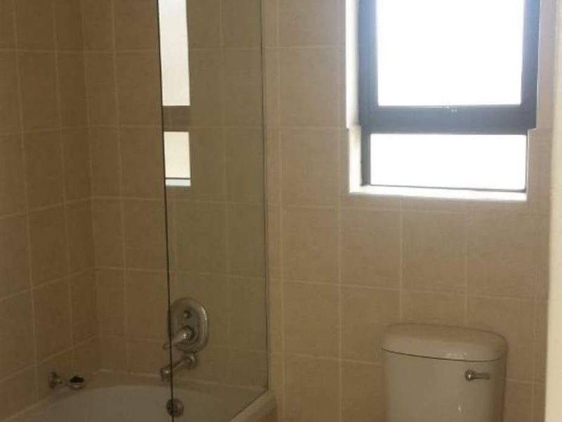 A functional bathroom featuring a bathtub with a glass shower screen, tiled walls, and a standard toilet.