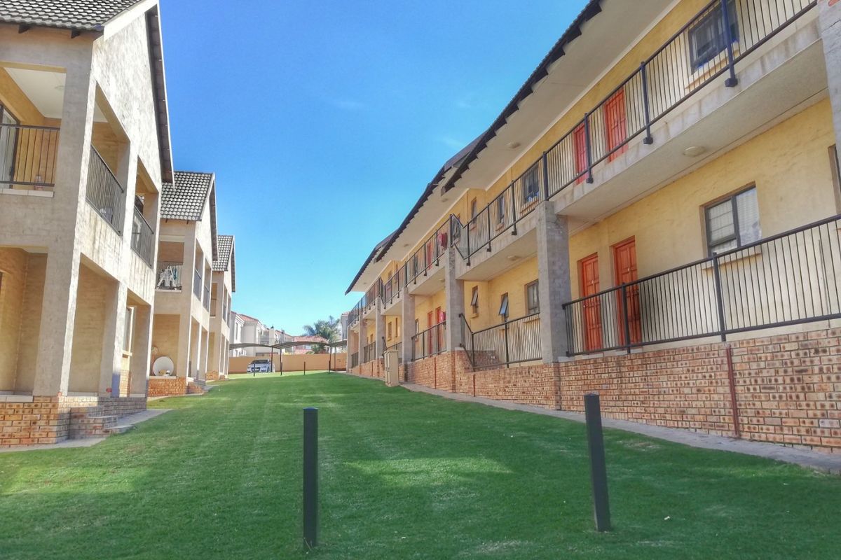 Exterior view of a multi-story apartment complex featuring brick base detailing, metal balcony railings, and a well-maintained communal lawn area between buildings.