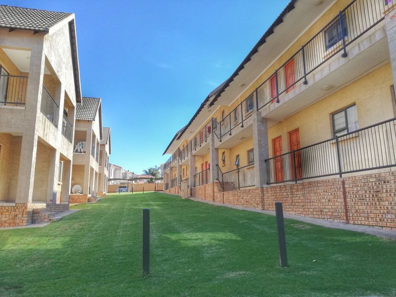 Exterior view of a multi-story apartment complex featuring brick base detailing, metal balcony railings, and a well-maintained communal lawn area between buildings.