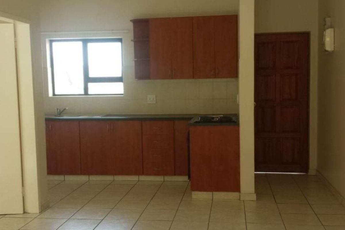 A functional kitchen featuring wooden cabinetry, laminate countertops, a built-in hob, and tiled flooring, offering a clean and practical space for culinary activities.
