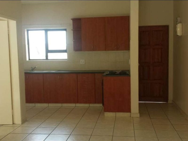 A functional kitchen featuring wooden cabinetry, laminate countertops, a built-in hob, and tiled flooring, offering a clean and practical space for culinary activities.