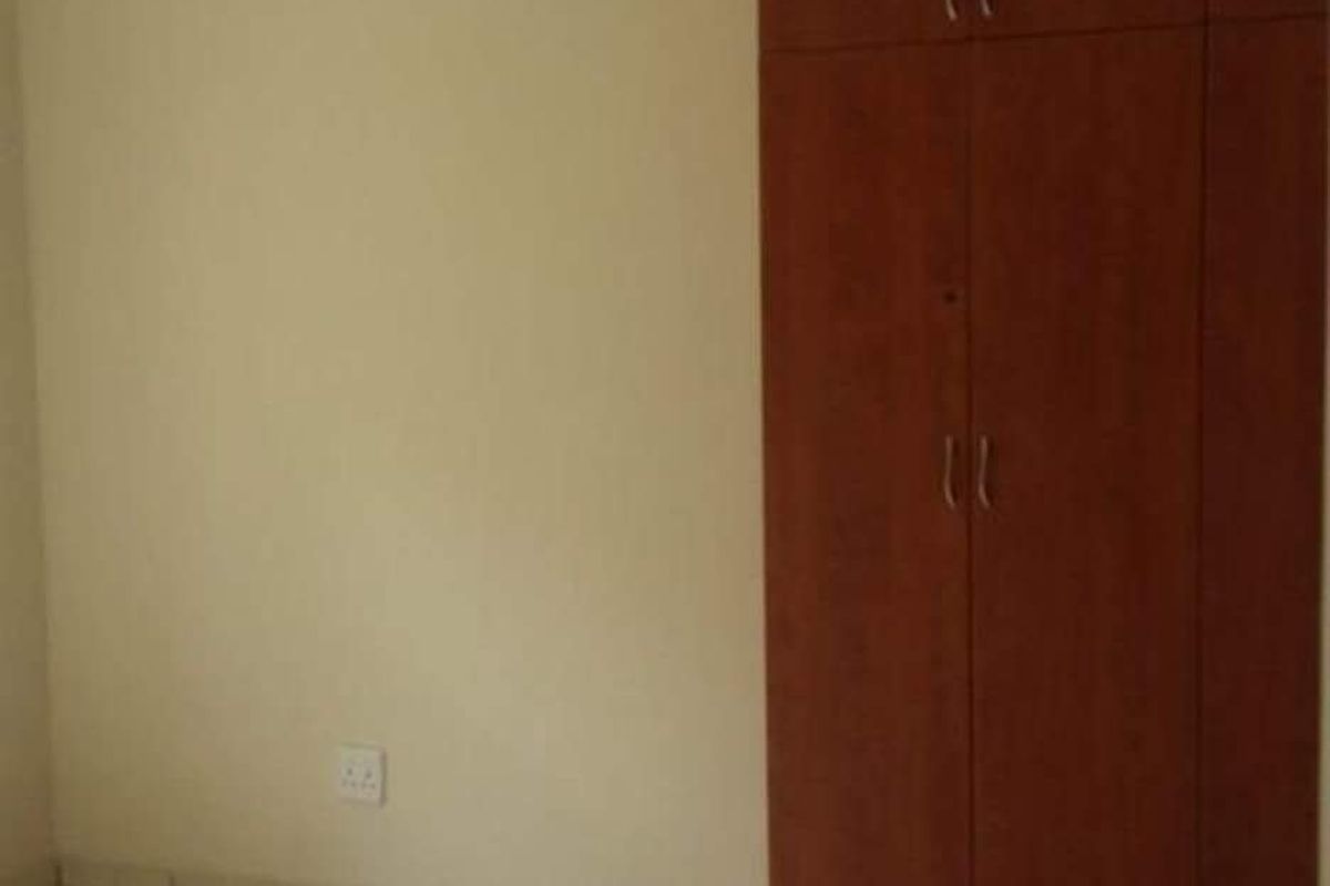 An empty bedroom featuring tiled flooring and a built-in wooden wardrobe.