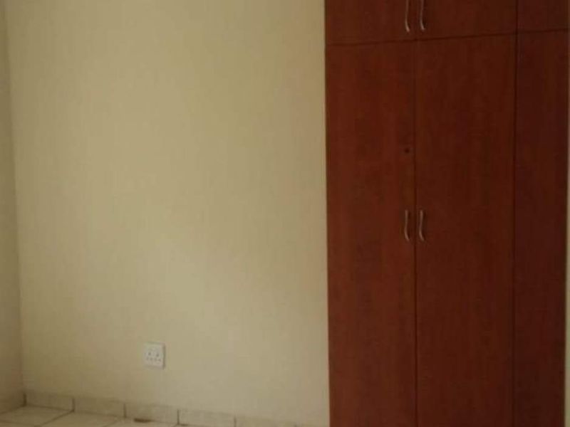 An empty bedroom featuring tiled flooring and a built-in wooden wardrobe.