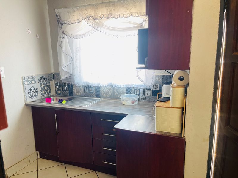 A compact kitchen area featuring dark wood-finish cabinetry, a stainless steel sink, patterned tiled splashback, and ceramic floor tiles.