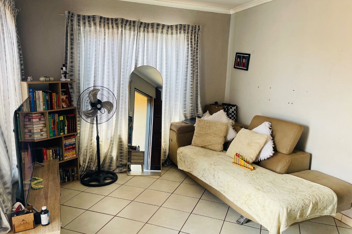 A living room featuring tiled flooring and large windows with curtain treatments, showing minor wall surface wear.