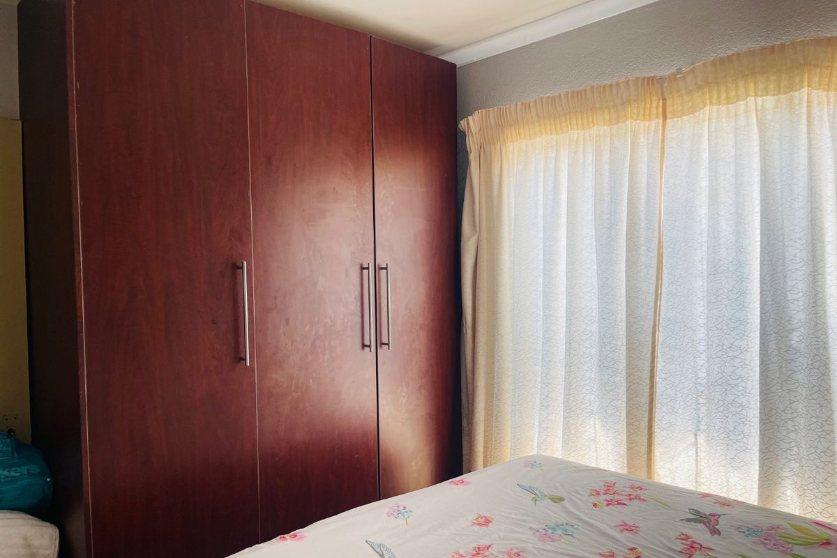 A bedroom featuring a large built-in wooden wardrobe and natural light filtering through window curtains.