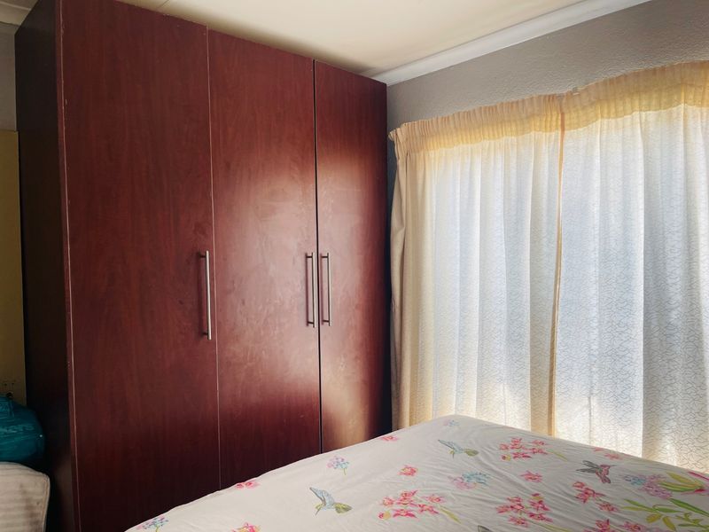 A bedroom featuring a large built-in wooden wardrobe and natural light filtering through window curtains.